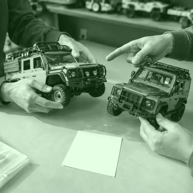 Dos personas comparando modelos RC sobre una mesa de trabajo